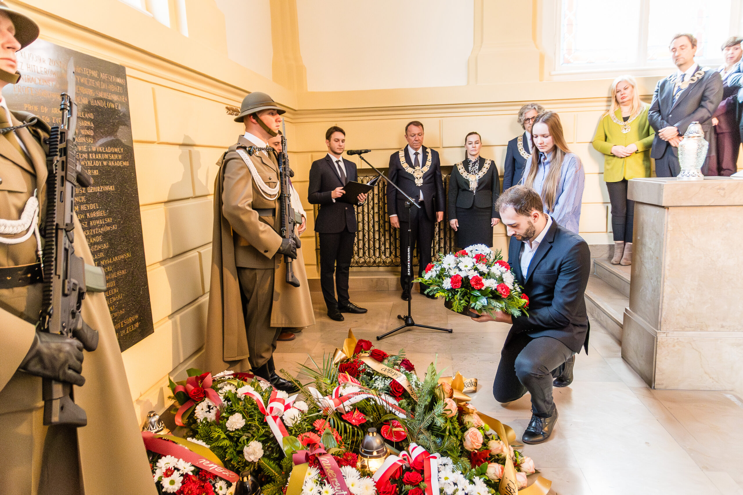 grupa osób na schodach, jedna skłąda wieniec